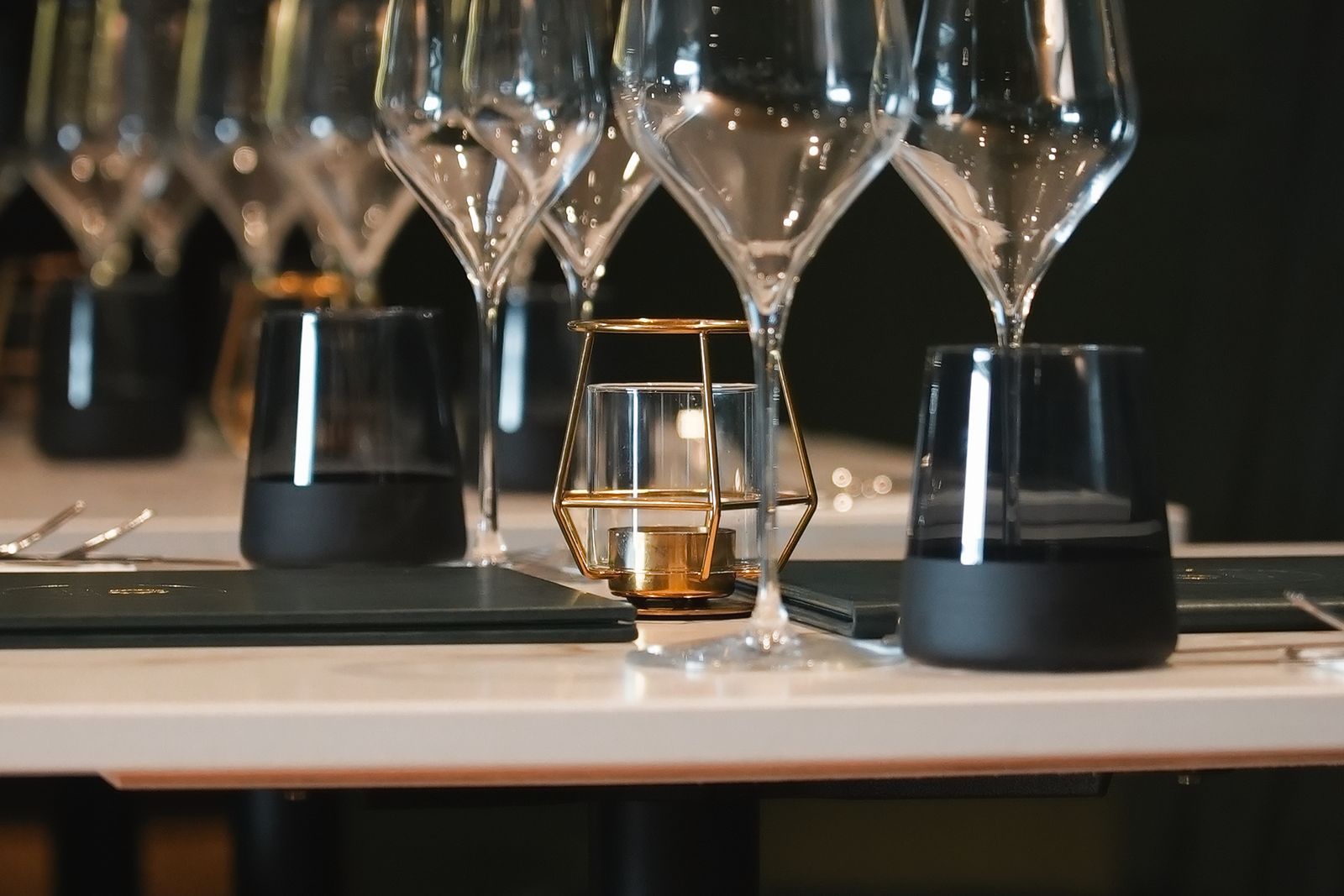 Wine glasses, smoked black tumblers and a brass tealight holder on a laid table